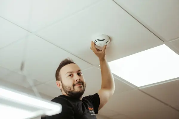Elektriker installiert Rauchmelder an einer Zimmerdecke für mehr Sicherheit im Gebäude.