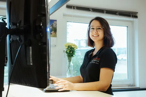 Freundliche Mitarbeiterin arbeitet am Computer im modernen Büro mit Fenster und Blumen.